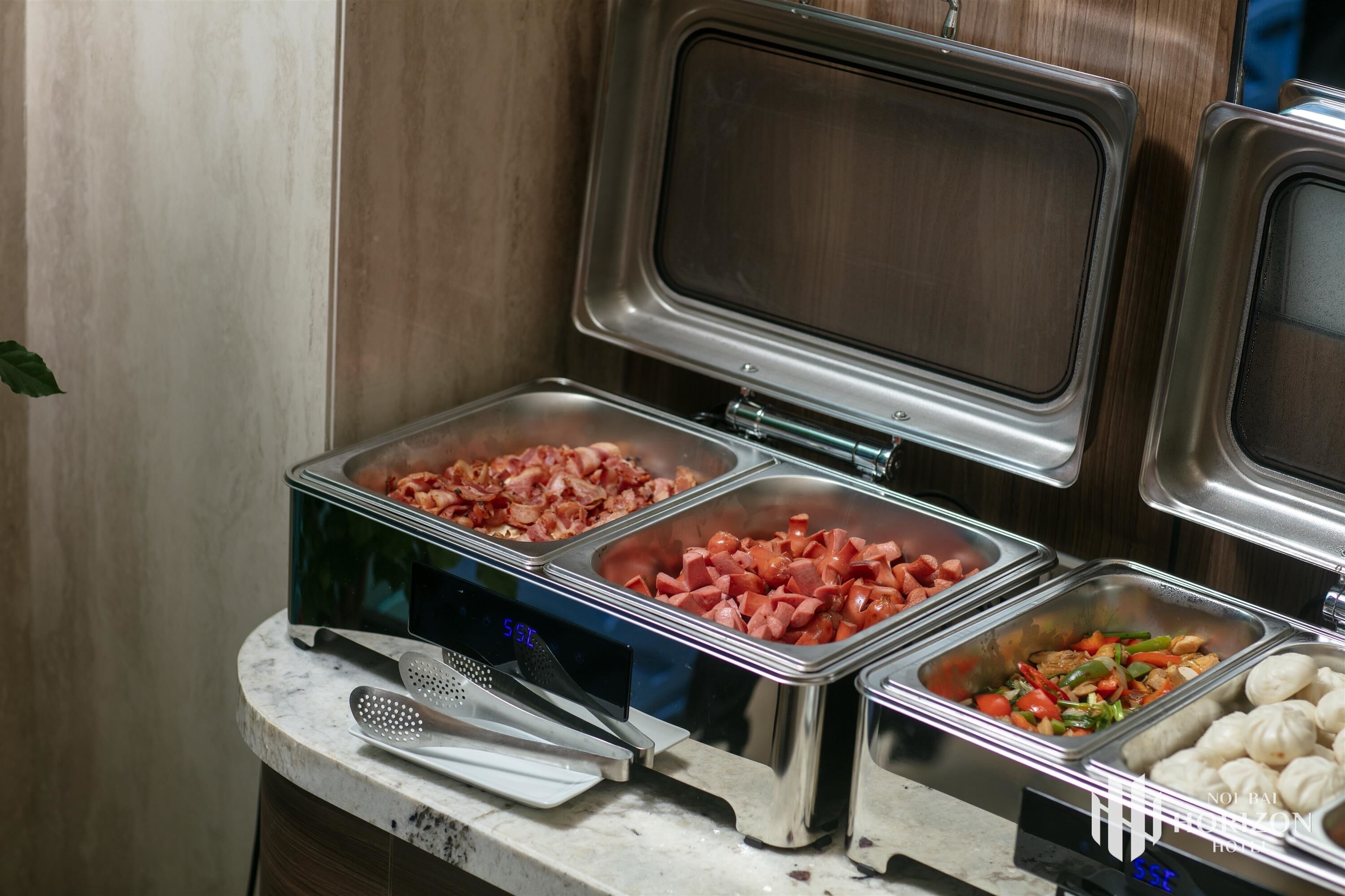 Een buffet met diverse gerechten, waaronder spek, worst en groenten.