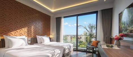Habitación de hotel con dos camas, un ventanal grande, un escritorio y vistas a edificios y zonas verdes.