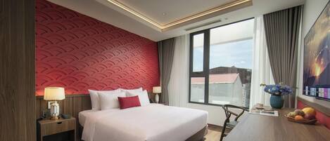 Ein Hotelzimmer mit einem großen Bett, einem Schreibtisch mit Stuhl, einem Fenster mit Aussicht und einer roten Wand mit Struktur.