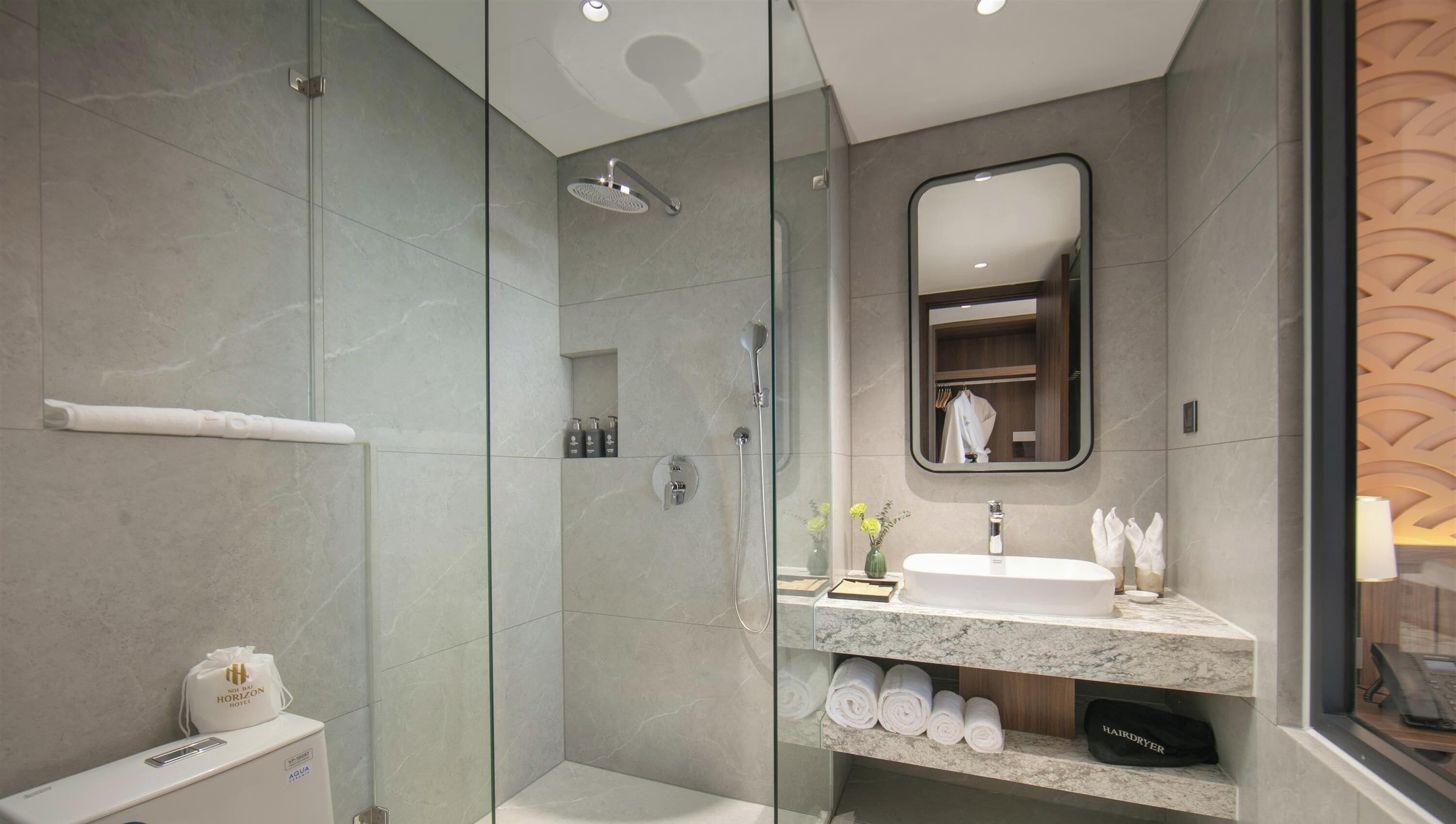A modern bathroom with a glass-enclosed shower, a marble sink, and neatly rolled towels.