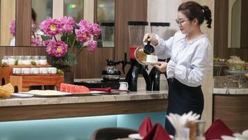 A person serving coffee in a restaurant with a counter, a flower arrangement, and neatly arranged tables and chairs.