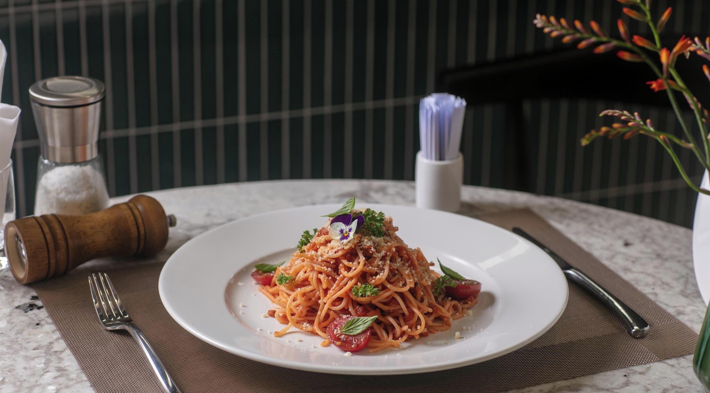 A plate of spaghetti with cherry tomatoes and basil on a marble table.