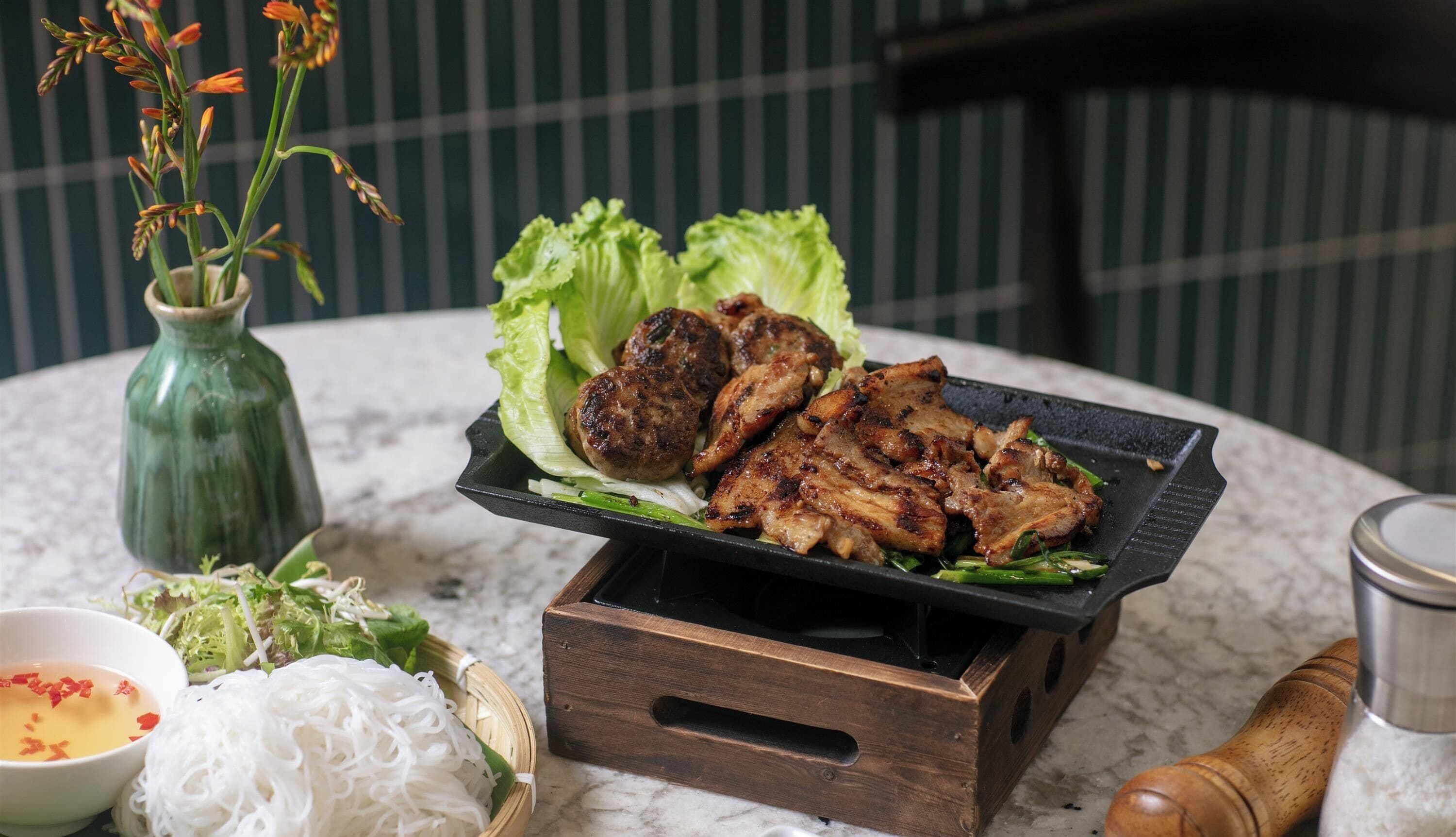 A table with grilled meat, lettuce, and a bowl of soup.
