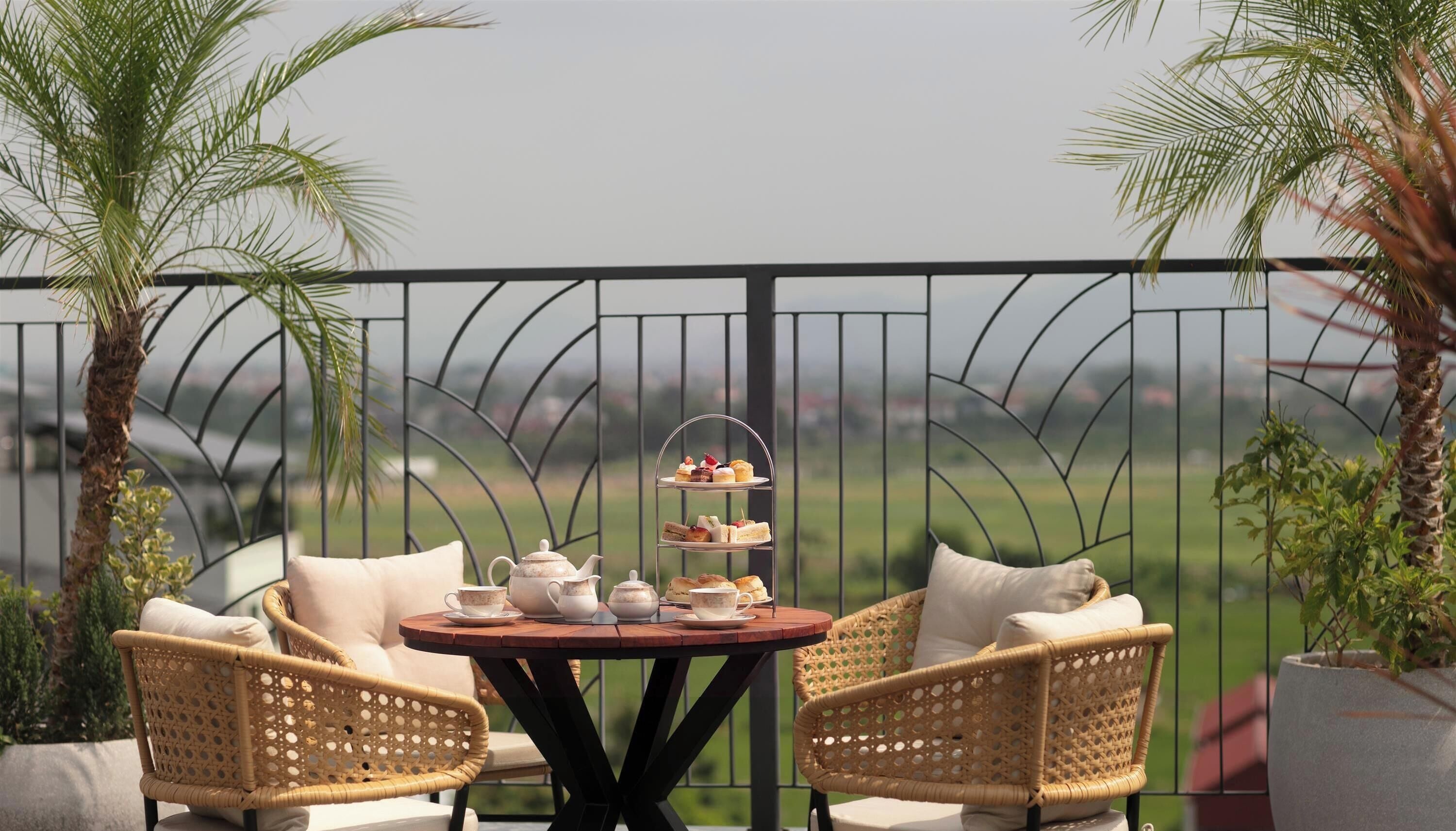 A balcony with a round table, wicker chairs, and a tiered tray of pastries.