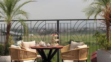 A balcony with a round table, wicker chairs, and a tiered tray of pastries.