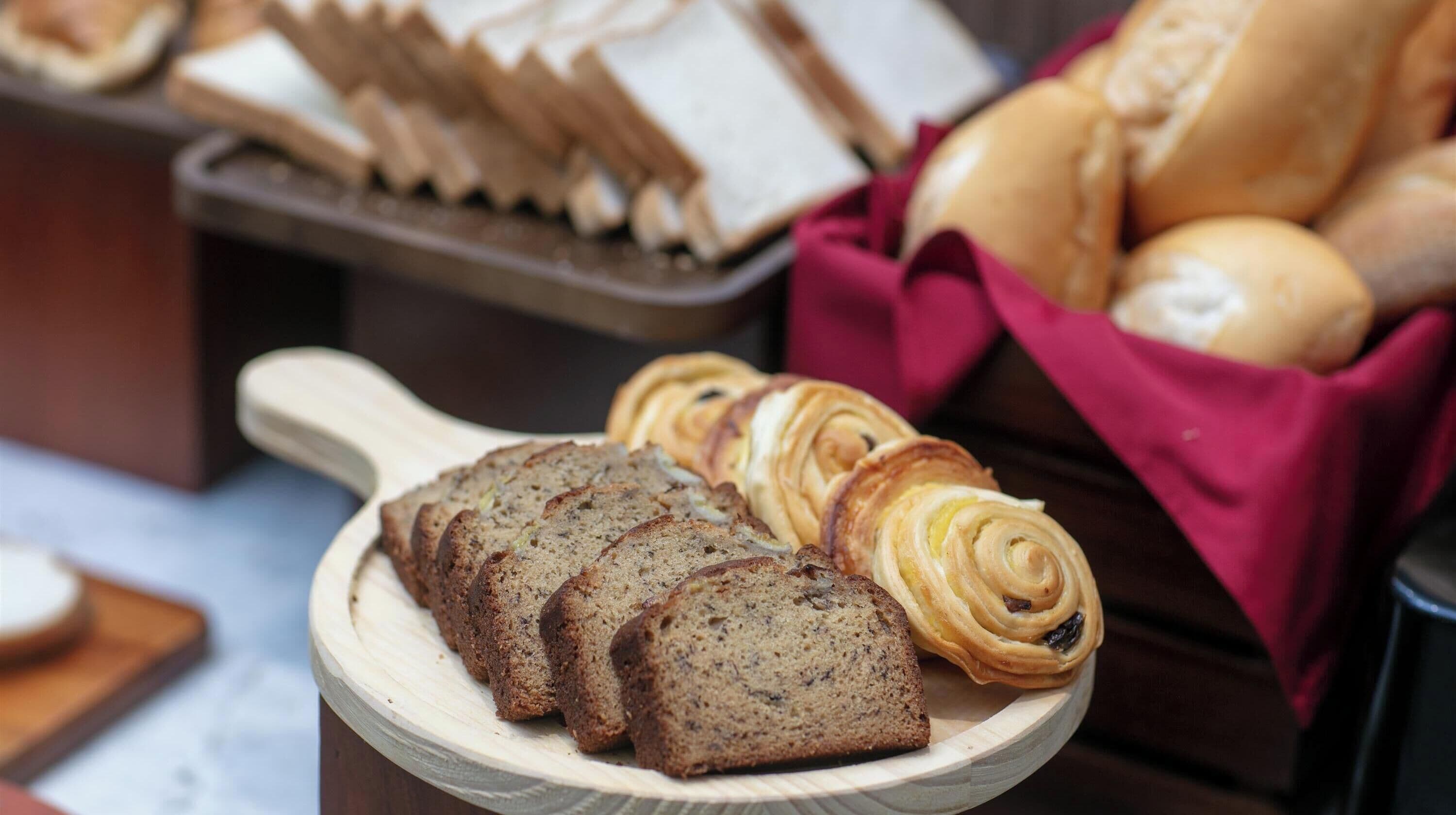 A wooden serving board with sliced bread and pastries.