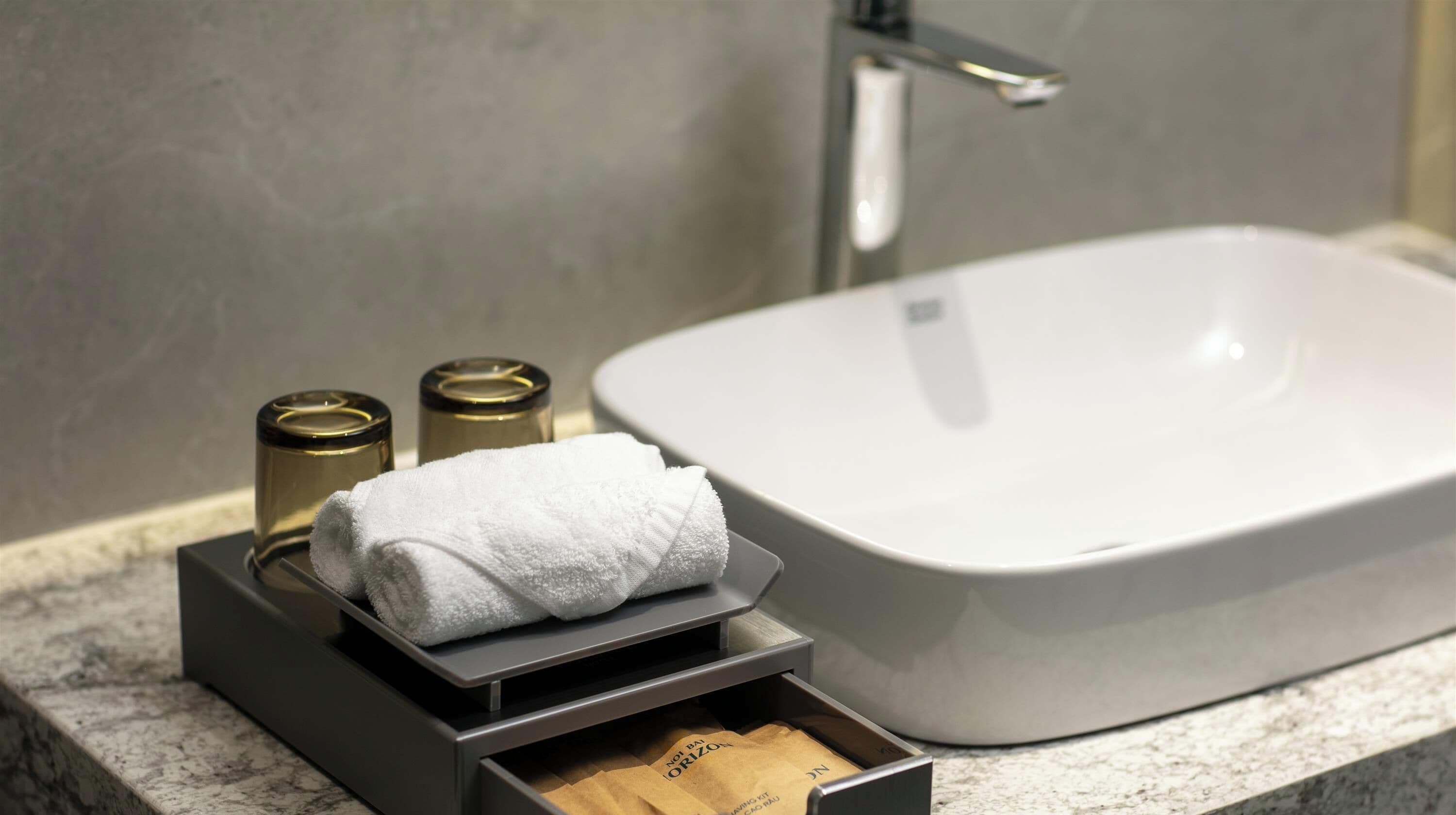 A bathroom with a white sink, a towel, and two containers on a marble countertop.