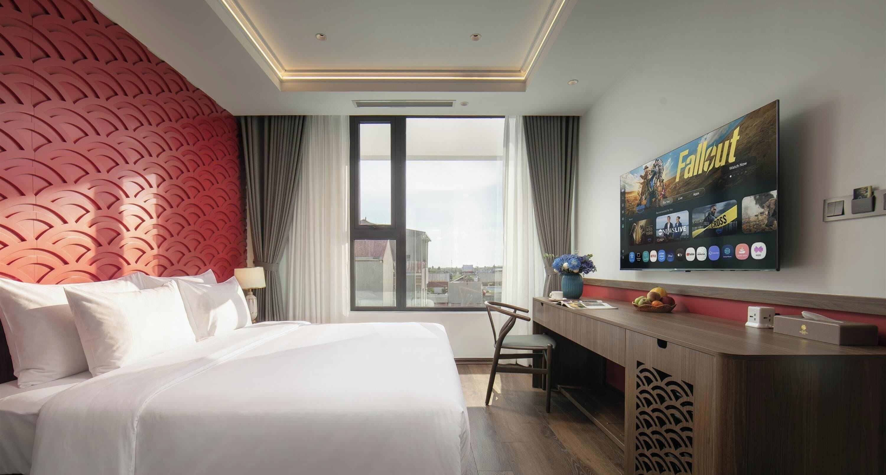 Ein Hotelzimmer mit einem großen Bett, einem Schreibtisch, einem Fernseher und Blick auf die Stadt durch das Fenster.