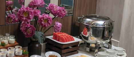 Montaje de desayuno buffet con diversos alimentos, una presentación de frutas y un jarrón decorativo con flores.