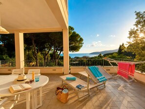 A sunlit outdoor seating area with a table, chairs, and lounge chairs, overlooking a scenic landscape. - Vrbo Property (Capoliveri)