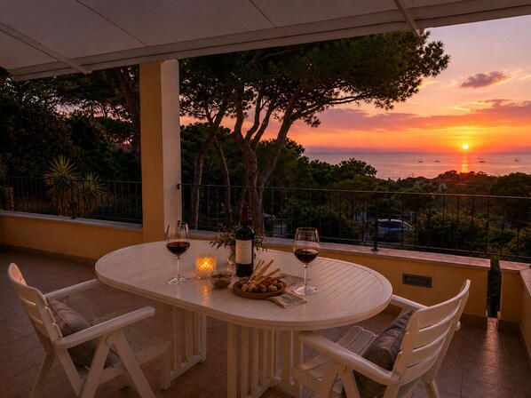A round table with white chairs, a bottle of wine, two wine glasses, a candle, and a bowl of bread on a balcony overlooking a sunset and the sea. - House with a view of the sea, sunsets over Corsica and Pianosa, 700 meters from Spiaggia degli Stecchi (Capoliveri)