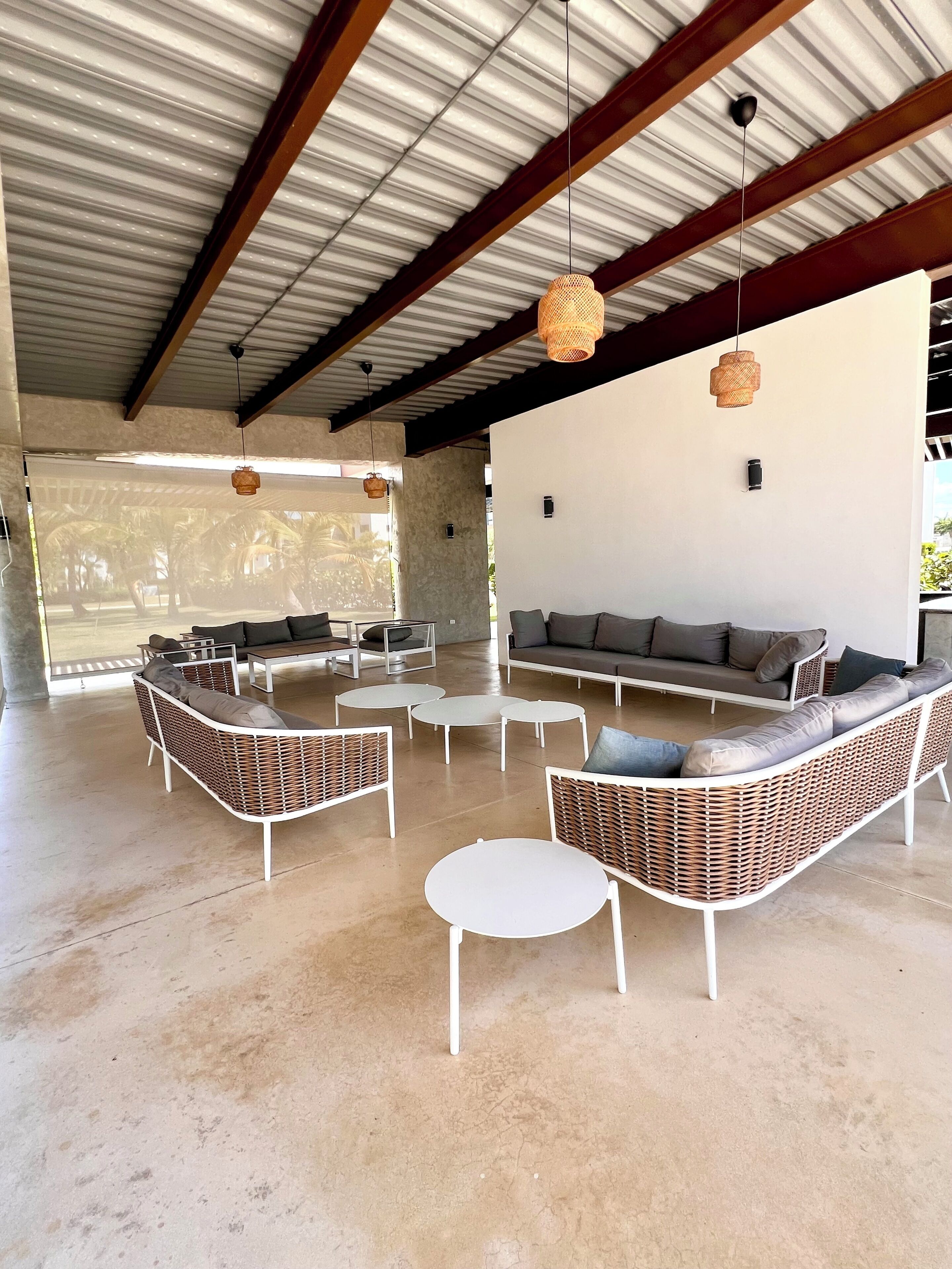 Un espace intérieur spacieux, aménagé avec des meubles en osier, un canapé blanc et des lampes en osier suspendues.