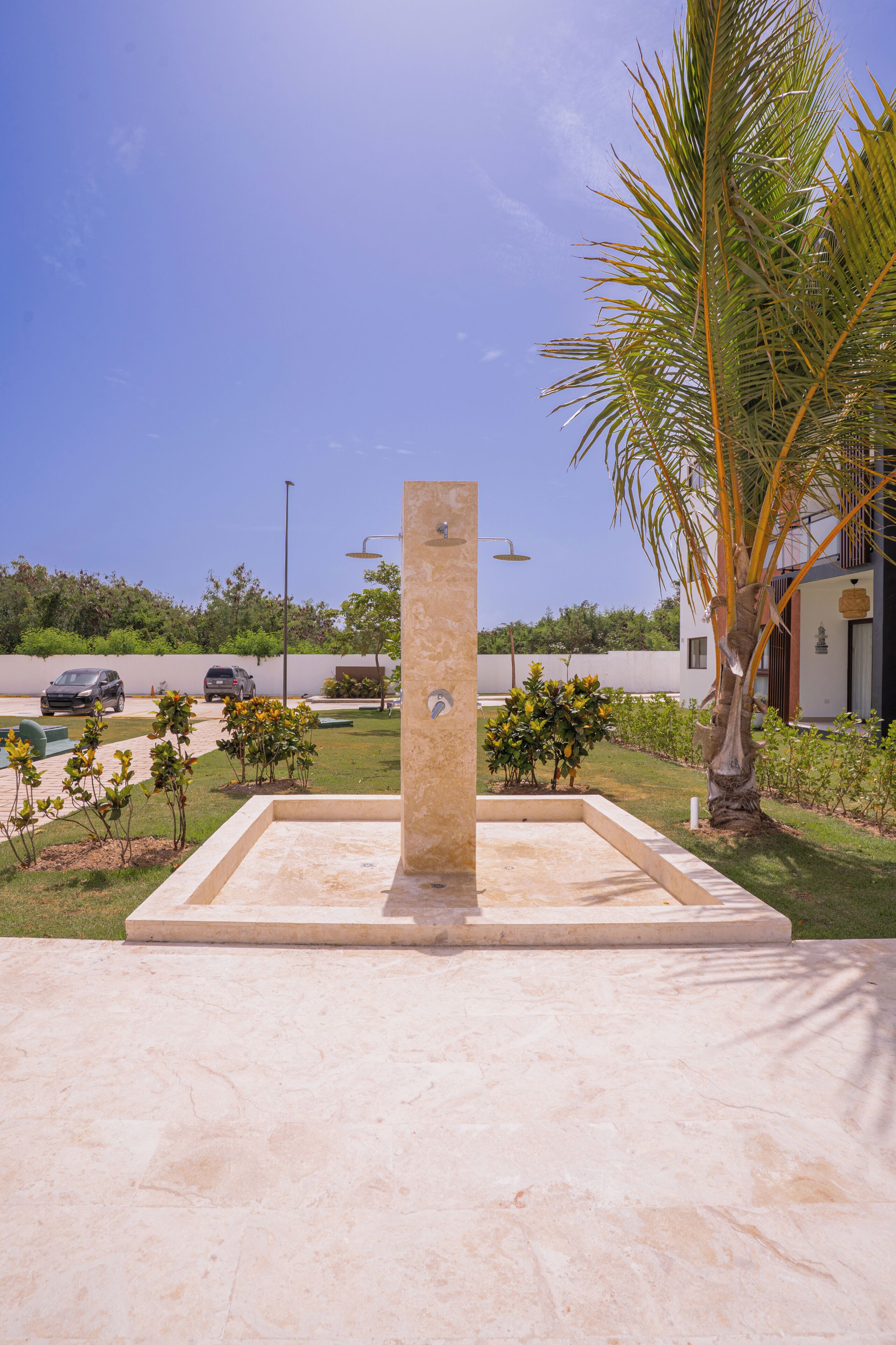 A concrete structure with a water feature, surrounded by a landscaped area with palm trees and shrubs.