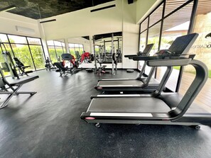 Een fitnessruimte met loopbanden, krachttrainingsapparatuur en een groot raam met uitzicht op groen.
