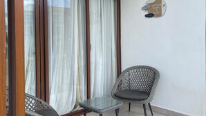 A balcony with two wicker chairs, a glass table, and a sliding glass door with curtains. - Haven Escape  2-bedroom condo with AC and private beach access in Punta Cana (Punta Cana)