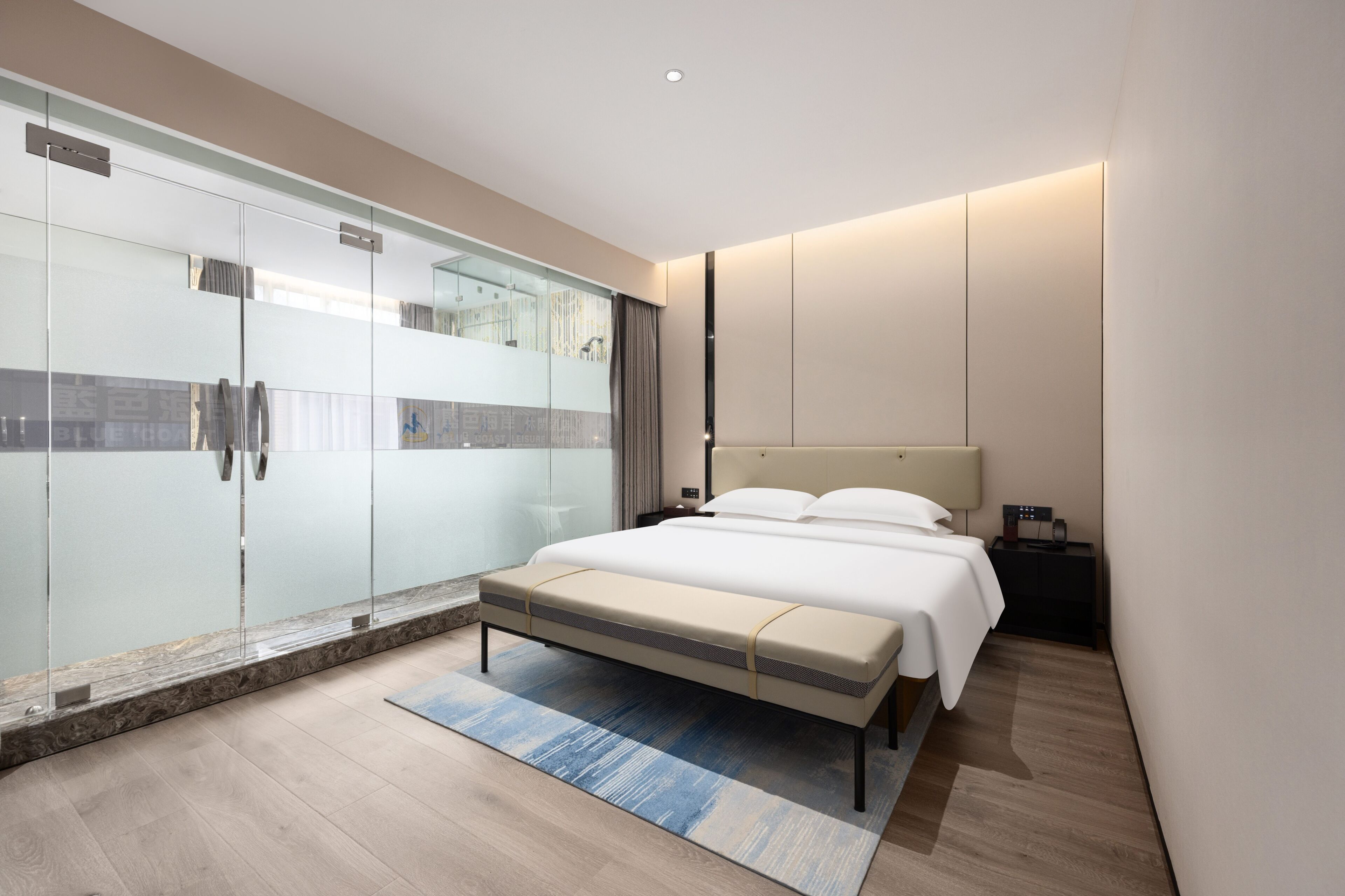 A modern bedroom with a glass shower enclosure, a large bed with a headboard, and a bedside table.