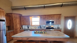 Una cocina con armarios de madera, un refrigerador de acero inoxidable, una isla grande con taburetes y un microondas sobre la encimera.