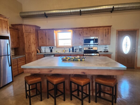 A kitchen with wooden cabinets, a stainless steel refrigerator, a large island with stools, and a microwave above the counter.