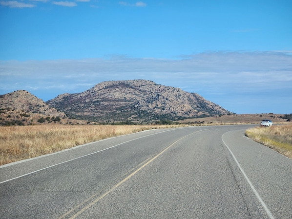 Una carretera serpentea por un paisaje árido y montañoso, con poca vegetación y una montaña al fondo.