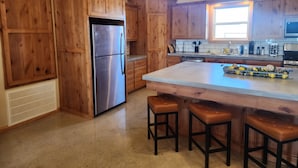 Cocina con armarios de madera, un refrigerador de acero inoxidable, una isla grande con taburetes y un ventanal que proporciona luz natural.