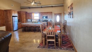 Una cocina amplia con armarios de madera, una isla central con taburetes de bar, una mesa de comedor con sillas y una araña.