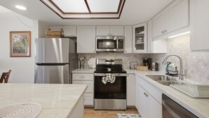 A modern kitchen with stainless steel appliances, white cabinetry, and a central island. - Brand-New Interior, 5-Min Walk to Beach, 2 Baths (Kihei)