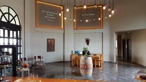 A spacious lobby with a bar area, wooden furniture, a large wine barrel centerpiece, and wall-mounted light fixtures. - Bakucha Vineyard Hotel ve Spa (Luleburgaz)