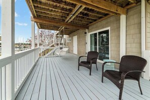 A wooden deck with two wicker chairs and a glass table, overlooking a marina.