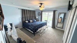 A bedroom with a bed, a ceiling fan, a window with curtains, a clock, and a view of the outside.