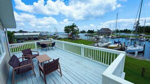 Eine Terrasse mit Gartenmöbeln, Blick auf eine Marina mit Booten und eine Rasenfläche.