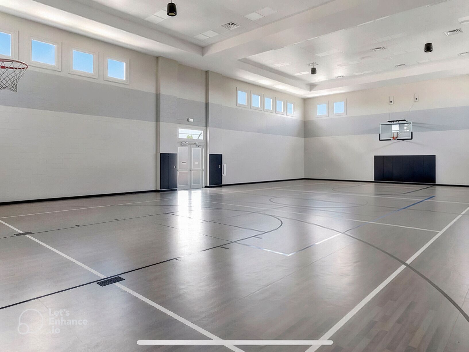 A spacious indoor basketball court with a high ceiling, multiple windows, and a basketball hoop.