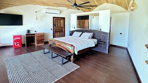 Een slaapkamer met een bed, een plafondventilator, een houten hoofdeinde, een bankje, een rode Coca-Cola koeler en een geweven plafond.