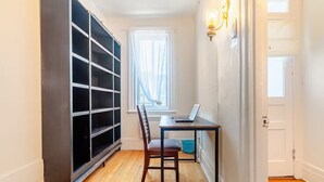 Une pièce avec un plancher en bois, un bureau avec un ordinateur portable, une chaise, une fenêtre avec des rideaux et une grande bibliothèque noire.