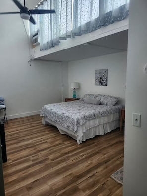 A bedroom with a bed, a ceiling fan, an air conditioning unit, a bedside lamp, and a wall-mounted artwork. - Unique Bishop Loft (Honolulu)