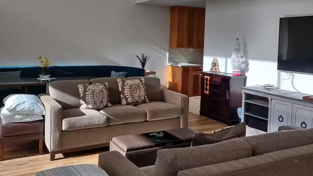 A modern living room with a high ceiling, a ceiling fan, a large flat-screen TV, and a decorative Christmas tree. - Unique Bishop Loft (Honolulu)