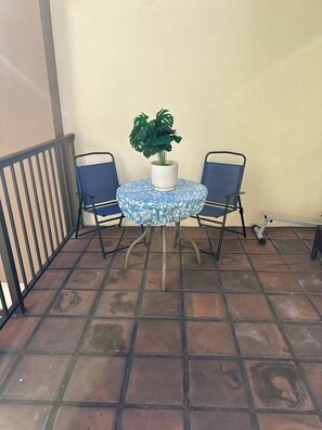 Ein runder Tisch mit blumigem, blauem Tischläufer, zwei blaue Stühle und ein Blumentopf.