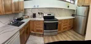 A kitchen with wooden cabinets, a stainless steel refrigerator, a built-in oven, and a marble countertop. - Unique Bishop Loft (Honolulu)