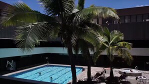 A swimming pool with a clear blue water surface, surrounded by palm trees and lounge chairs. - Unique Bishop Loft (Honolulu)