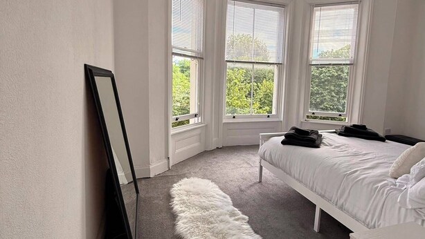 Une chambre à coucher avec un lit, un tapis blanc et moelleux, une table de chevet et un miroir au mur.