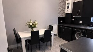 Une cuisine moderne avec des meubles de couleur noire, un plan de travail blanc et un coin repas comprenant une table et des chaises.