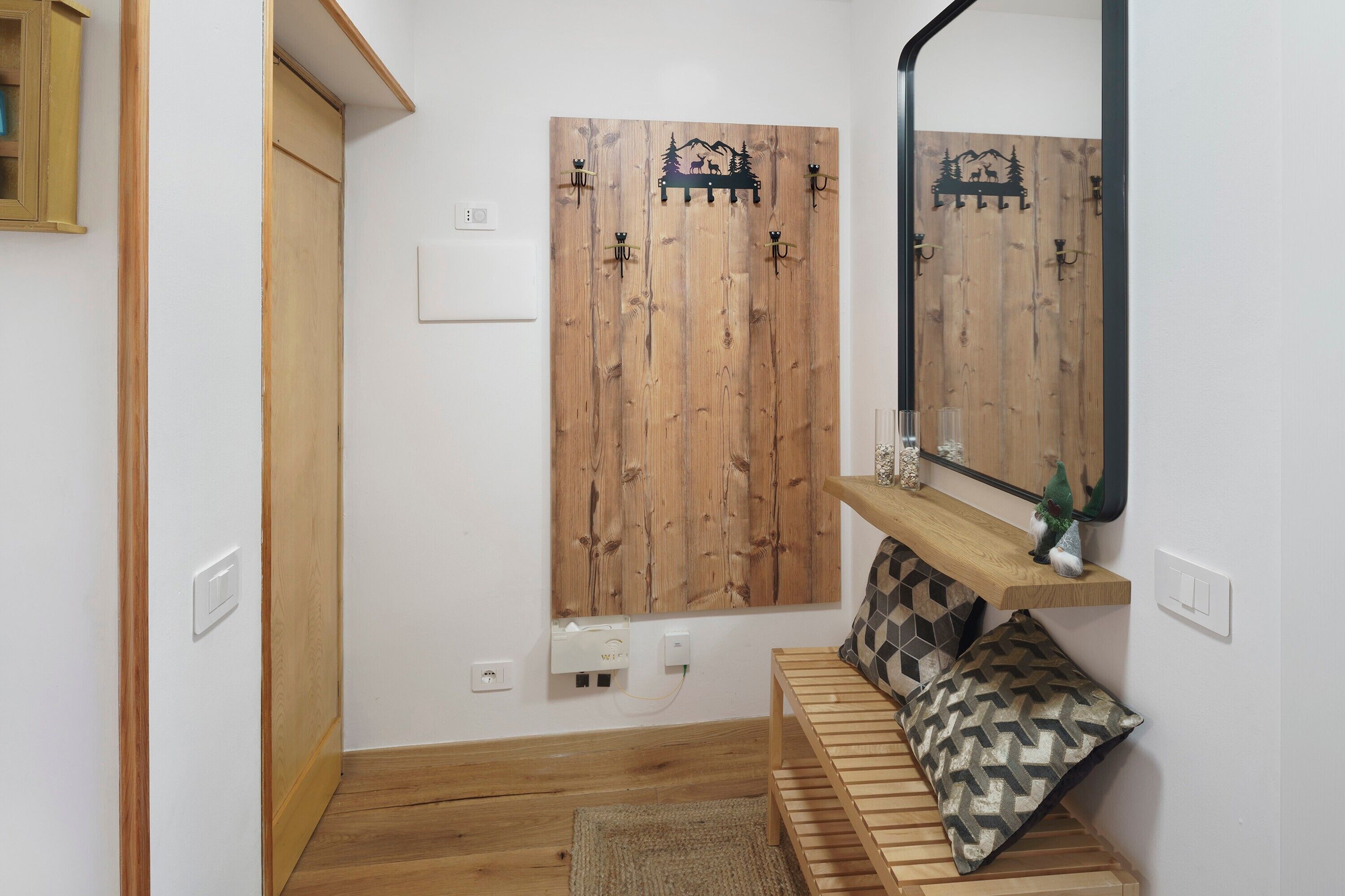 A bathroom with a wooden vanity, a mirror, a shelf with decorative items, and a patterned pillow on the floor.