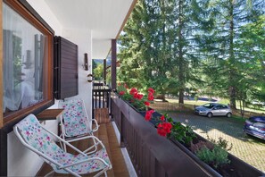 A balcony with two chairs, a wooden fence, and a row of red flowers.
