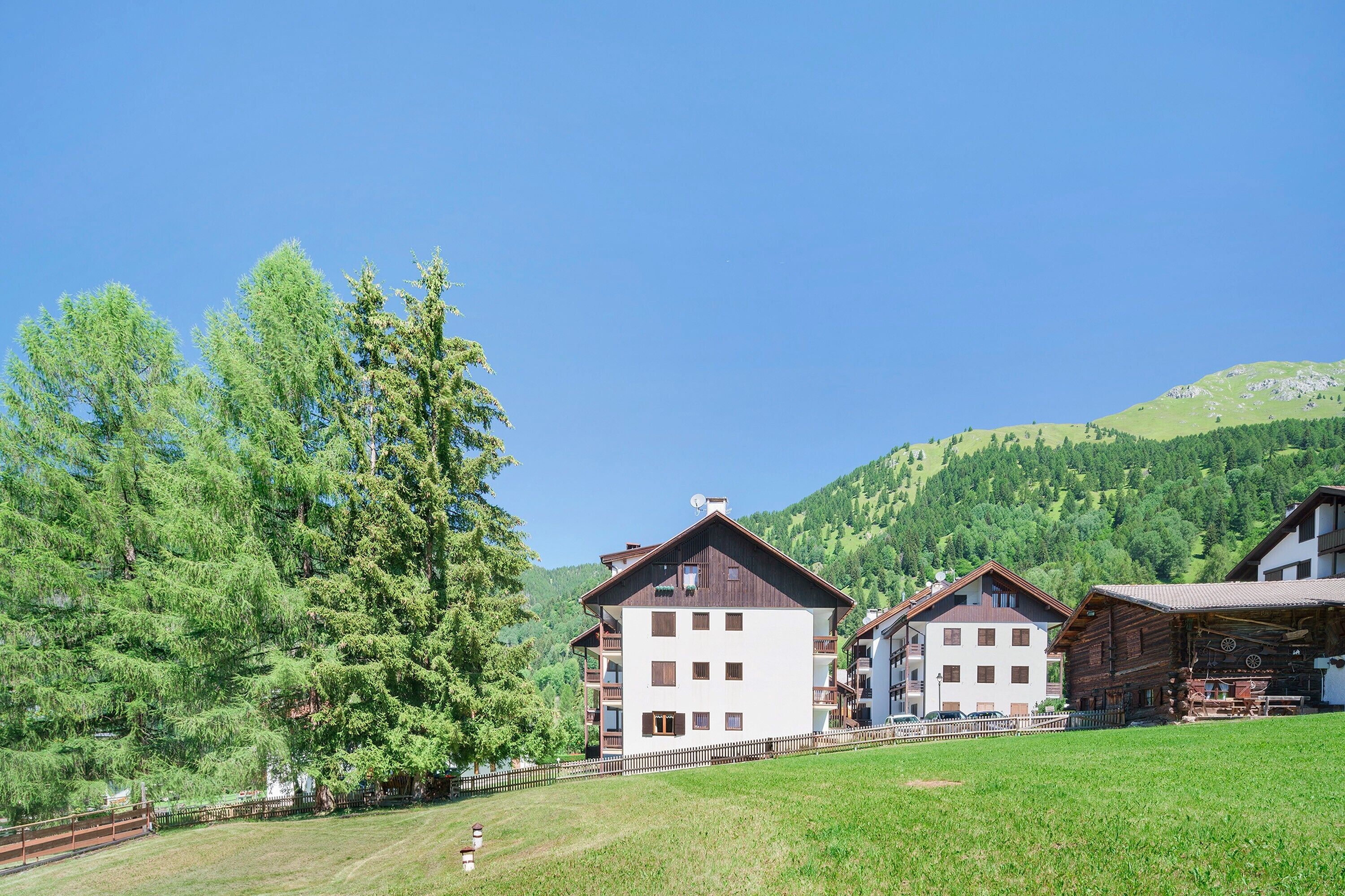 A row of traditional wooden buildings with balconies, set against a backdrop of green hills and clear blue sky.