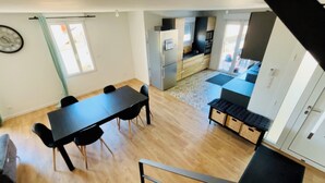 Una zona de menjador amb taula i caires, una cuina amb electrodomèstics i una escala.