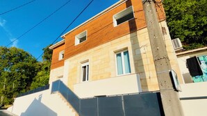 Un edifici de dues plantes amb façana de fusta, una planta baixa blanca i una escala visible.