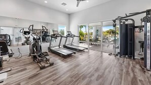 Ein Fitnessstudio mit Laufbändern, Kraftgeräten und einem Deckenventilator.