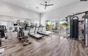 Ein Fitnessstudio mit Laufbändern, Kraftgeräten und einem Deckenventilator.
