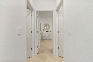 Ein Flur mit weißen Wänden und Türen, die zu einem Raum mit einem Spiegel und einem Zierteil führen.