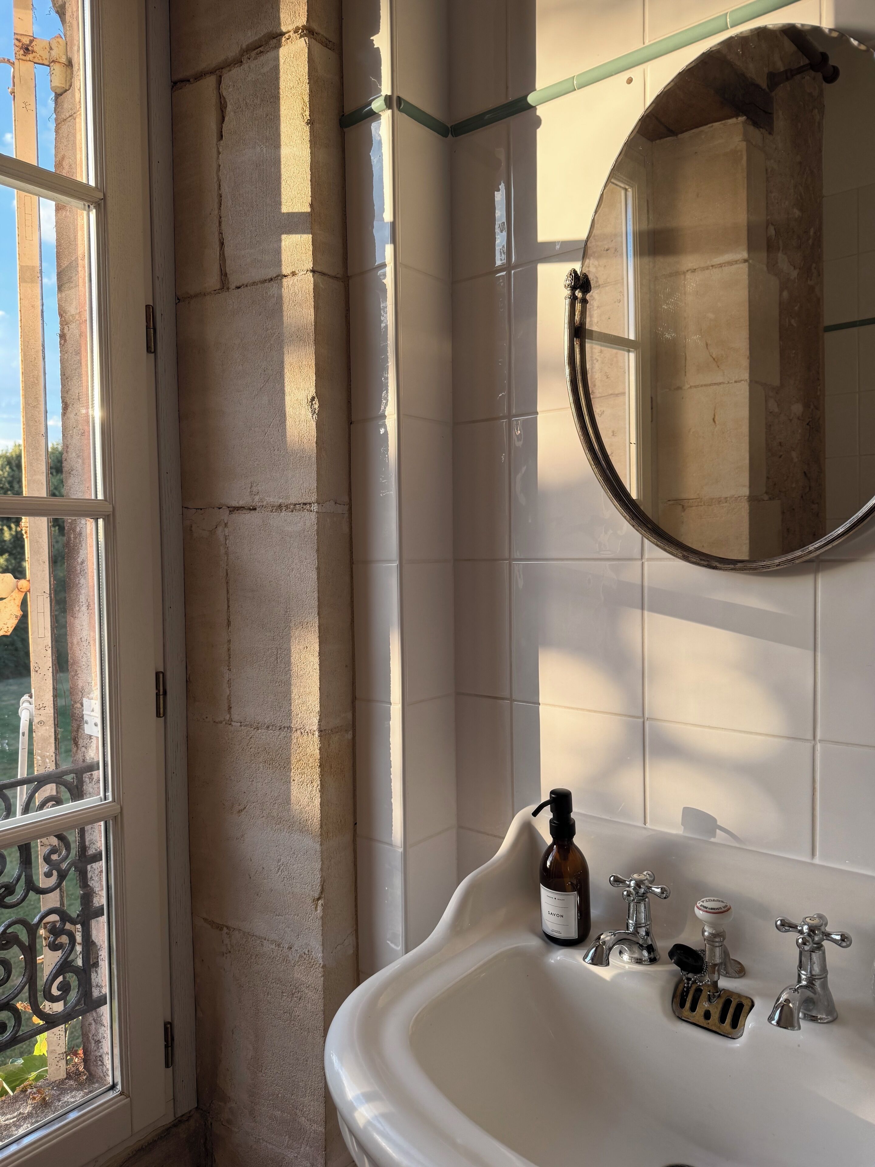 A bathroom with a white sink, a mirror, and a window with a view of greenery.