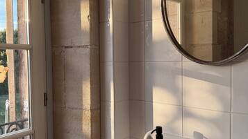 A bathroom with a white sink, a mirror, and a window with a view of greenery.